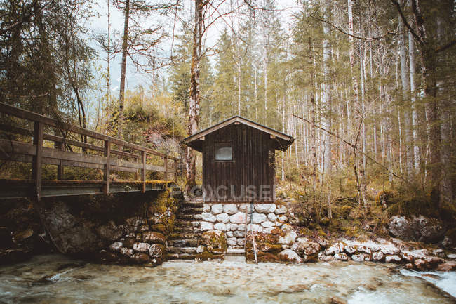 Small wooden cabin on stone shore of fast creek in tranquil woods. — Stock Photo