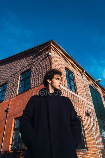 Молодой человек в пальто позирует на солнечной улице — стоковое фото