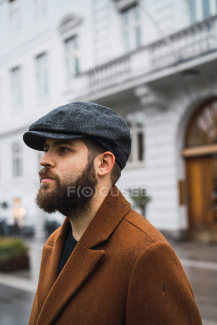 Vista lateral do homem confiante em boné e casaco andando na rua — Fotografia de Stock