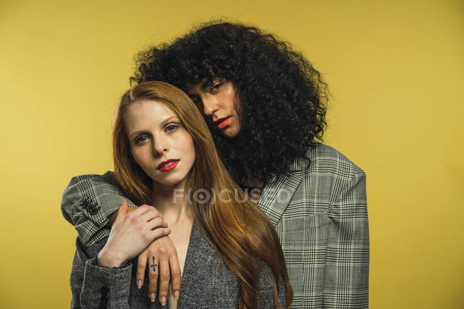 Two women embracing and looking at camera on yellow background — Stock Photo