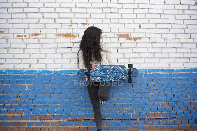Brunette girl posing with longboard and leaning on brick wall — Stock Photo