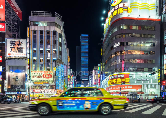 Gelber Taxiwagen fährt nachts über Kreuzung in asiatischer Metropole. — Stockfoto