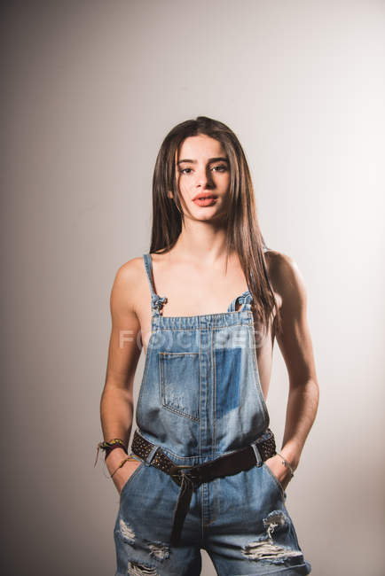 Brunette topless girl posing in denim overall and looking at camera — Stock Photo