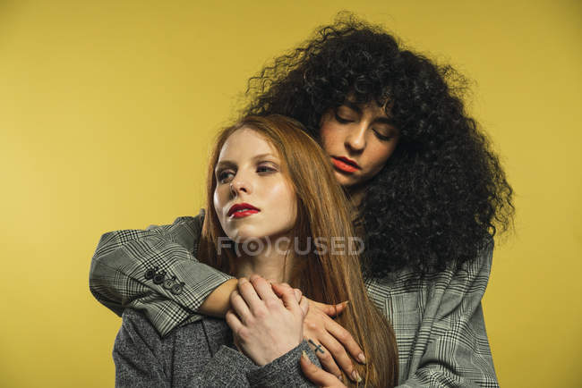 Zwei junge Frauen, die sich auf gelbem Hintergrund umarmen. — Stockfoto
