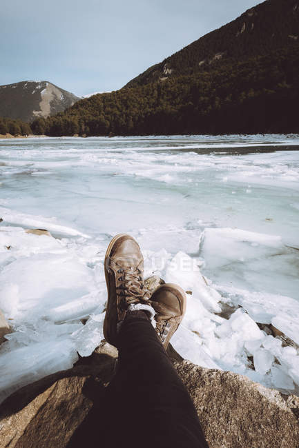 Baixa seção de turista sentado e descansando e rio gelado nevado em montanhas . — Fotografia de Stock