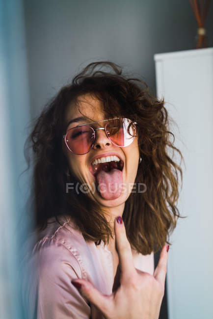 Portrait de femme en veste et lunettes de soleil grimacant et montrant un geste rock — Photo de stock