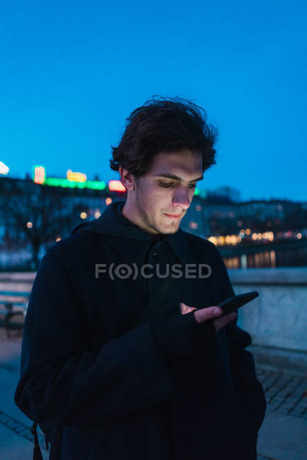 Retrato de homem que navega smartphone enquanto caminha na rua à noite — Fotografia de Stock