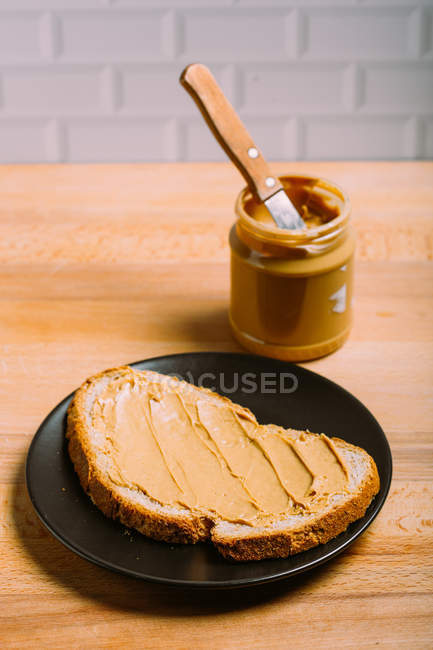 Vista de cerca del sándwich de mantequilla de maní en el plato por frasco de mantequilla de maní - foto de stock