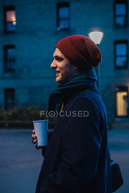 Side view of man in warm clothes walking on street with coffee — Stock Photo