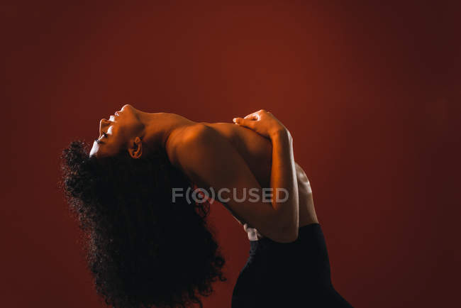 Вид сбоку кудрявой безтонной женщины, позирующей на красном фоне в студии . — стоковое фото