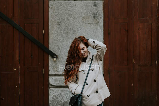 Rossa donna in posa sulla strada e toccare i capelli — Foto stock
