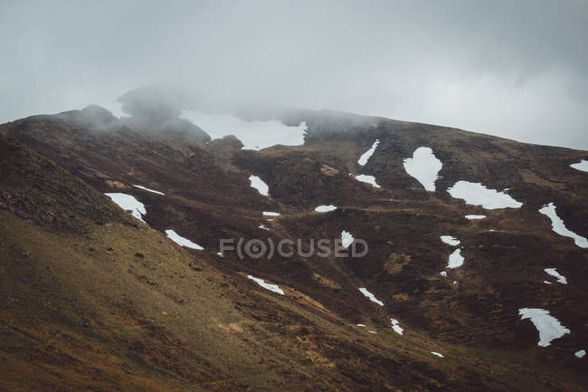 Montaña verde con nieve bajo el cielo nublado - foto de stock