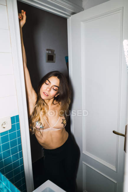 Молода жінка в бюстгальтері спирається на дверний проріз у ванній — стокове фото