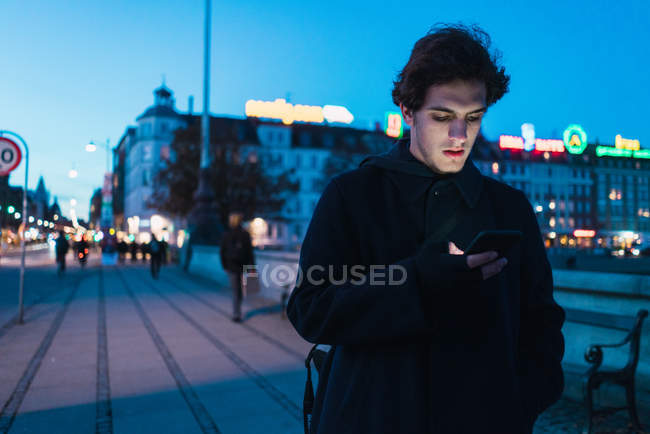 Мужчина просматривает смартфон на вечерней улице — стоковое фото