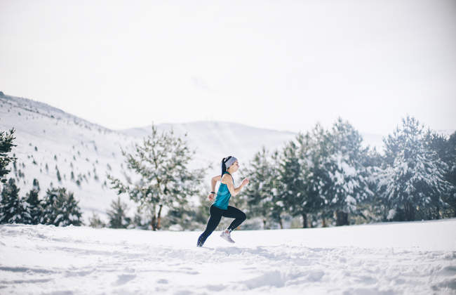 Vista lateral de la mujer corriendo en el campo cubierto de nieve - foto de stock