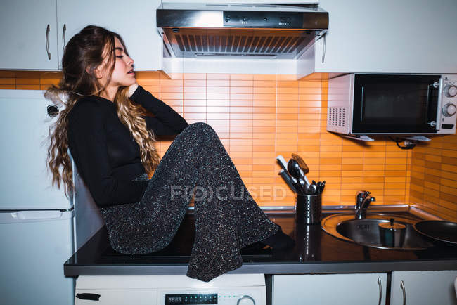 Vista laterale della giovane donna seduta sul tavolo della cucina — Foto stock