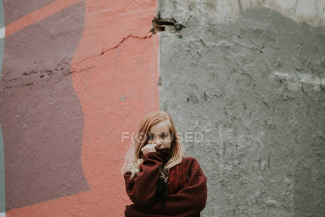 Блондинка в свитере позирует у потрепанной стены — стоковое фото