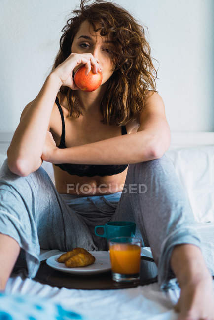 Приваблива жінка з яблуком сидить за підносом на сніданок на ліжку — стокове фото