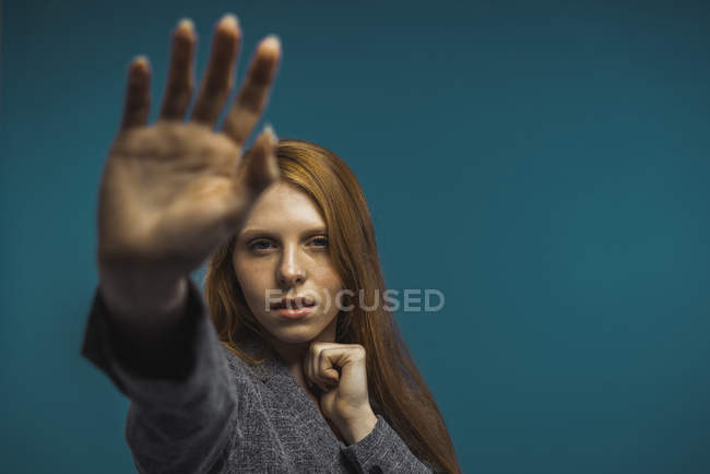 Молода приваблива жінка показує знак руки і дивиться на камеру на синьому фоні . — стокове фото