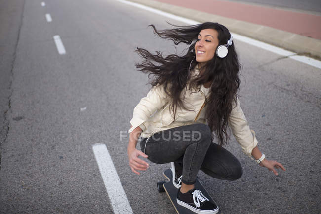 Молодая девушка в наушниках катается на длинной доске по асфальтовой дороге — стоковое фото