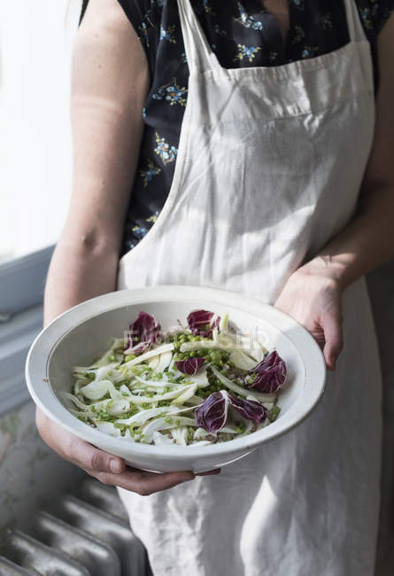 Sezione centrale della donna in grembiule contenente ciotola di insalata mista fresca . — Foto stock