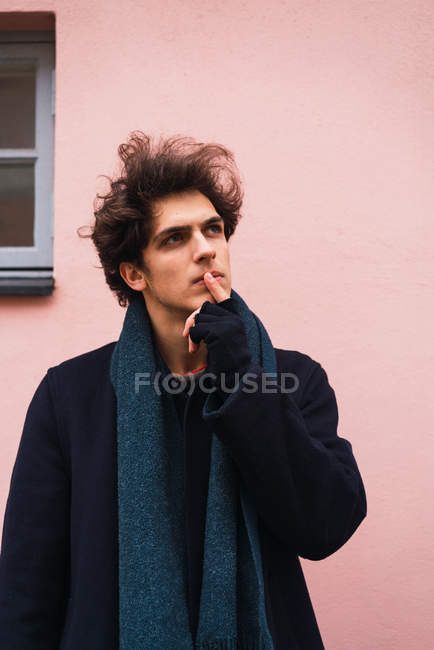 Thoughtful young man touching lips and looking up on city street. — Stock Photo