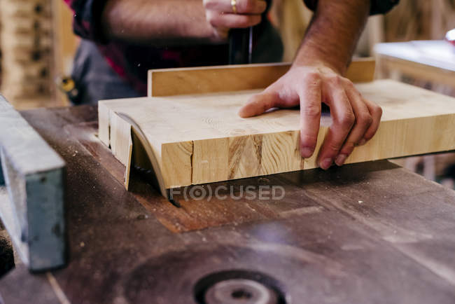 Crop carpenter cutting piece of wood with circle saw — Stock Photo