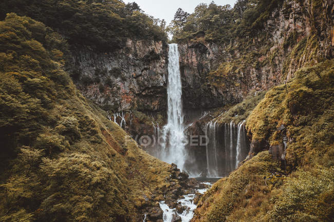 Vista idilliaca di una grande cascata che scorre tra le montagne verdi . — Foto stock