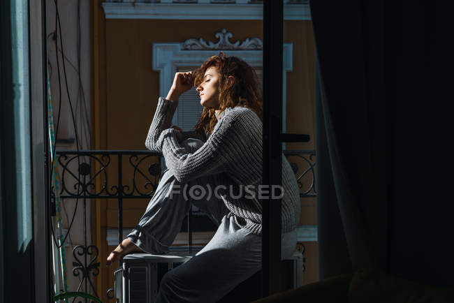 Vista lateral da jovem mulher sentada na varanda e relaxante com os olhos fechados . — Fotografia de Stock