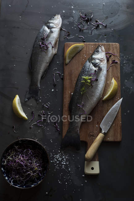 Raw sea bass on wooden board with lemon slices and knife — Stock Photo