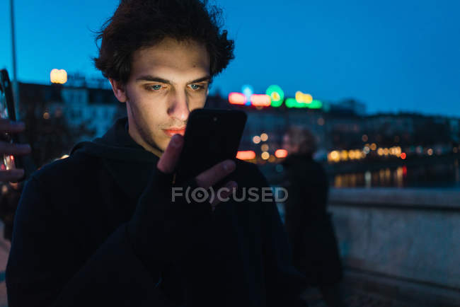 Man browsing smartphone in evening street scene — Stock Photo