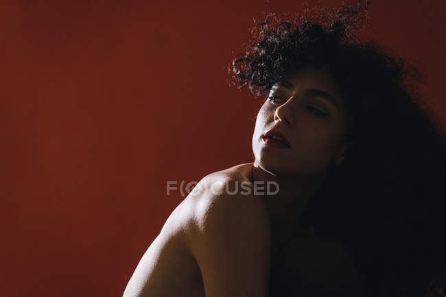 Jolie femme seins nus regardant par-dessus l'épaule sur fond rouge — Photo de stock