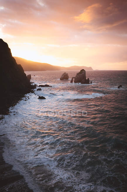 View to rocky coast and ocean waves in sunset lights. — Stock Photo