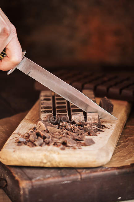 Mano de la cosecha con cuchillo de corte tabletas de chocolate en tablero de madera - foto de stock