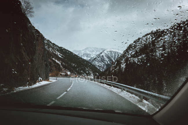 Vista a las colinas nevadas y camino de asfalto vacío desde el coche . - foto de stock