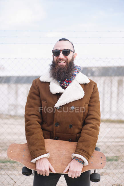 Portrait d'homme barbu en lunettes de soleil tenant skateboard — Photo de stock