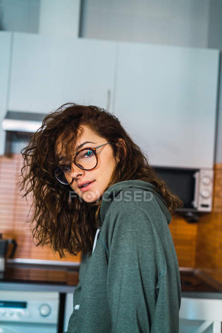 Mujer atractiva posando en la cocina y mirando a la cámara - foto de stock