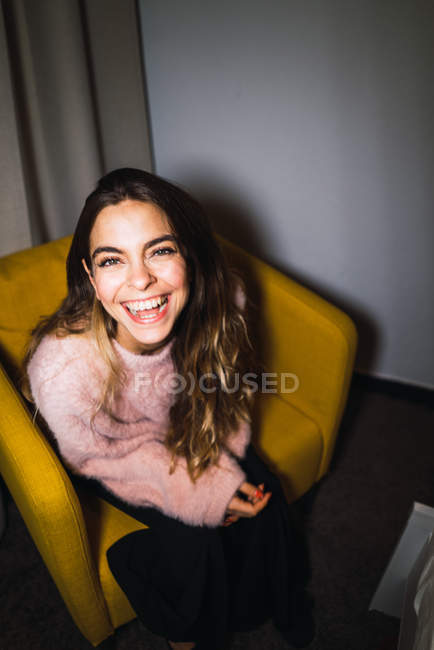 Lachende Frau auf Sessel sitzend und in Kamera blickend — Stockfoto