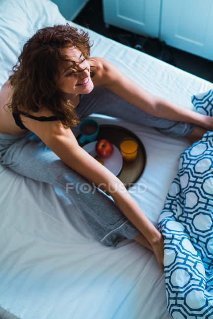 Mulher bonita esticando na cama com café da manhã — Fotografia de Stock