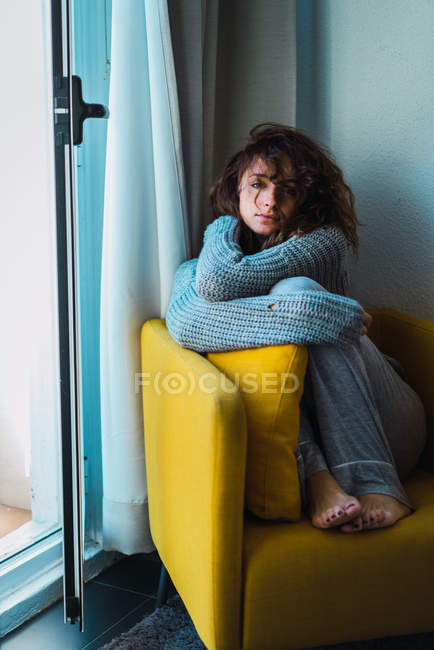 Frau sitzt mit Beinen im Sessel und blickt in die Kamera — Stockfoto