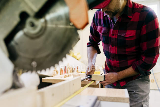 Cropped carpenter taking measure in piece of wood at workbench — Stock Photo