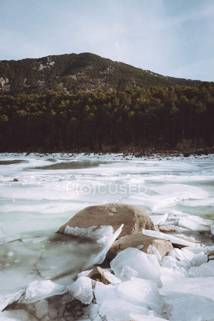 Zugefrorener eisiger Fluss und bewaldeter Hügel. — Stockfoto