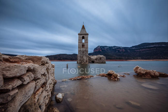Torre de sino submersa em lago calmo sob paisagem dramática — Fotografia de Stock