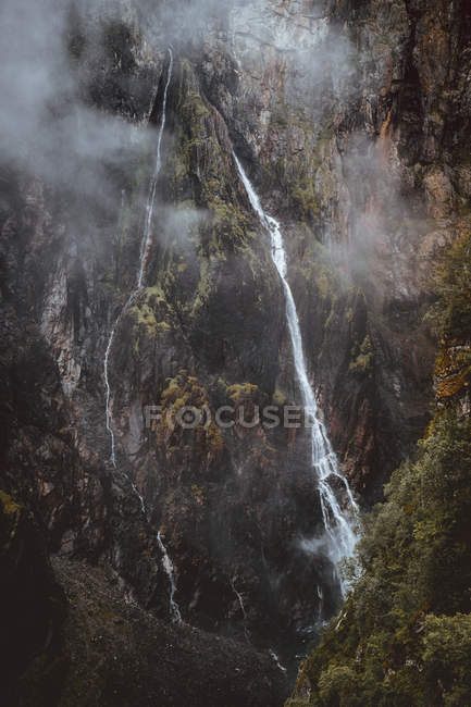 Aerial view to thin small waterfall in green high mountains. — Stock Photo