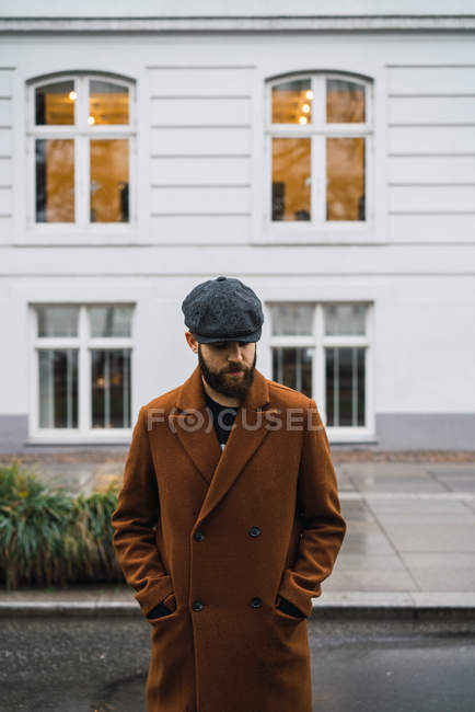 Портрет бородатого человека в винтажном пальто и кепке, смотрящего вниз на улицу — стоковое фото