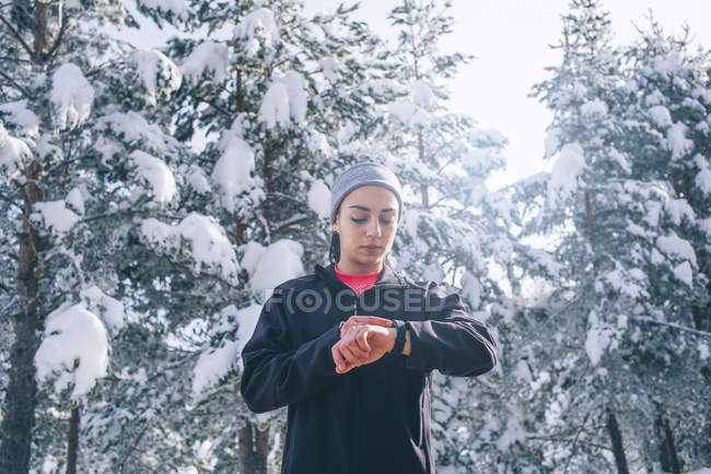Porträt einer fitten Frau beim Blick auf die Sportuhr im Winterwald — Stockfoto