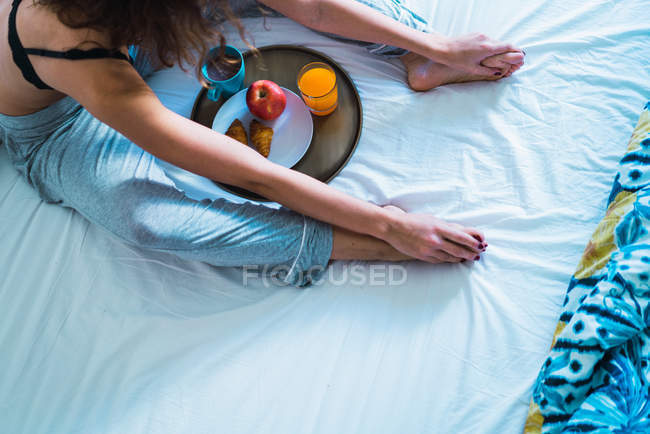 Женщина с урожая сидит на кровати с подносом, полным еды для завтрака . — стоковое фото