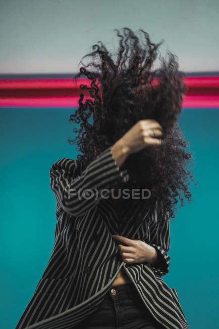 Curly brunette woman shaking hair on blue background — Stock Photo