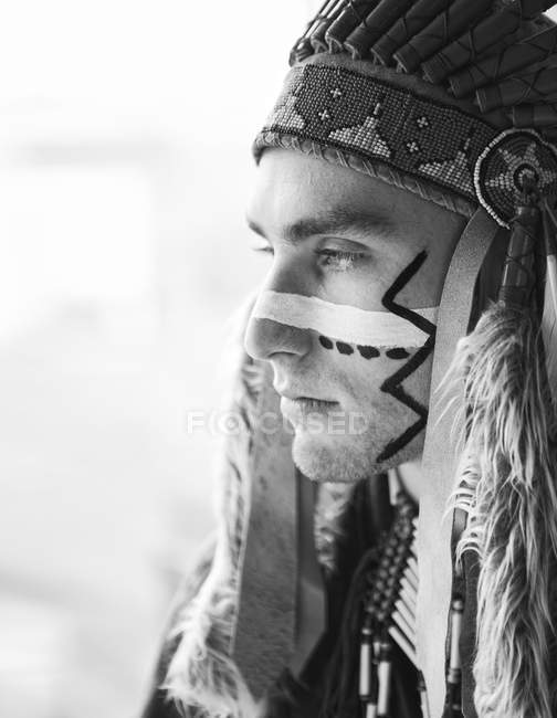 Side view of man with painted line on face posing in traditional Native American costume. — Stock Photo