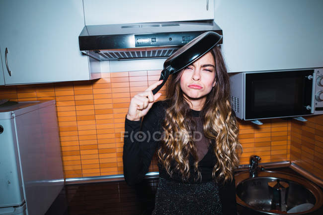 Young woman posing with pan on head on kitchen at home. — Stock Photo